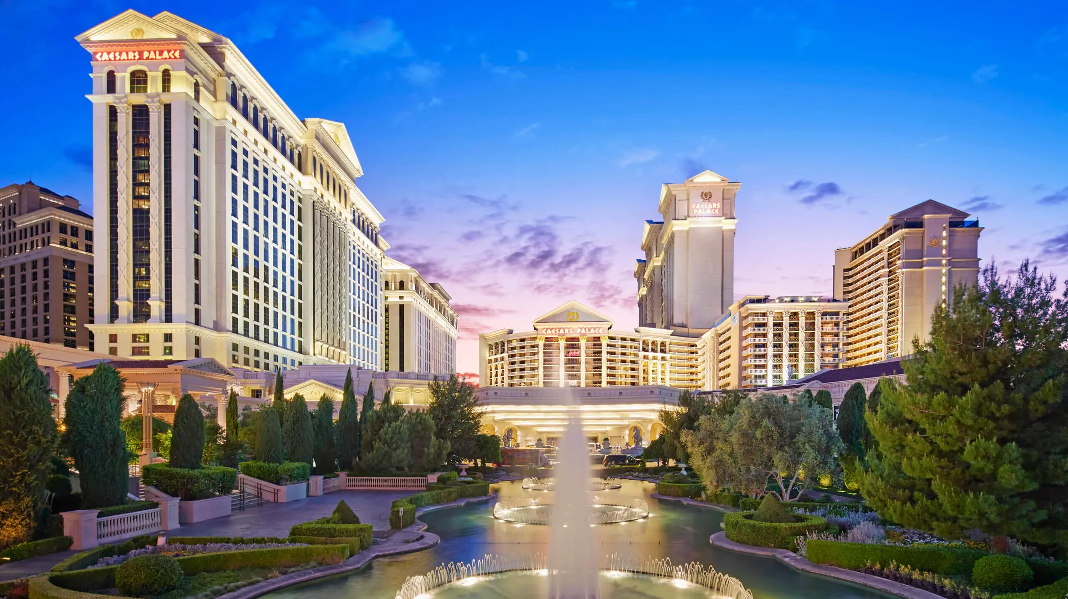 Wide exterior shot of the Caesars Palace hotel and casino complex in Las Vegas during twilight.