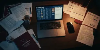 NFL scouting office desk with laptop, phone, and draft documents in dramatic lighting