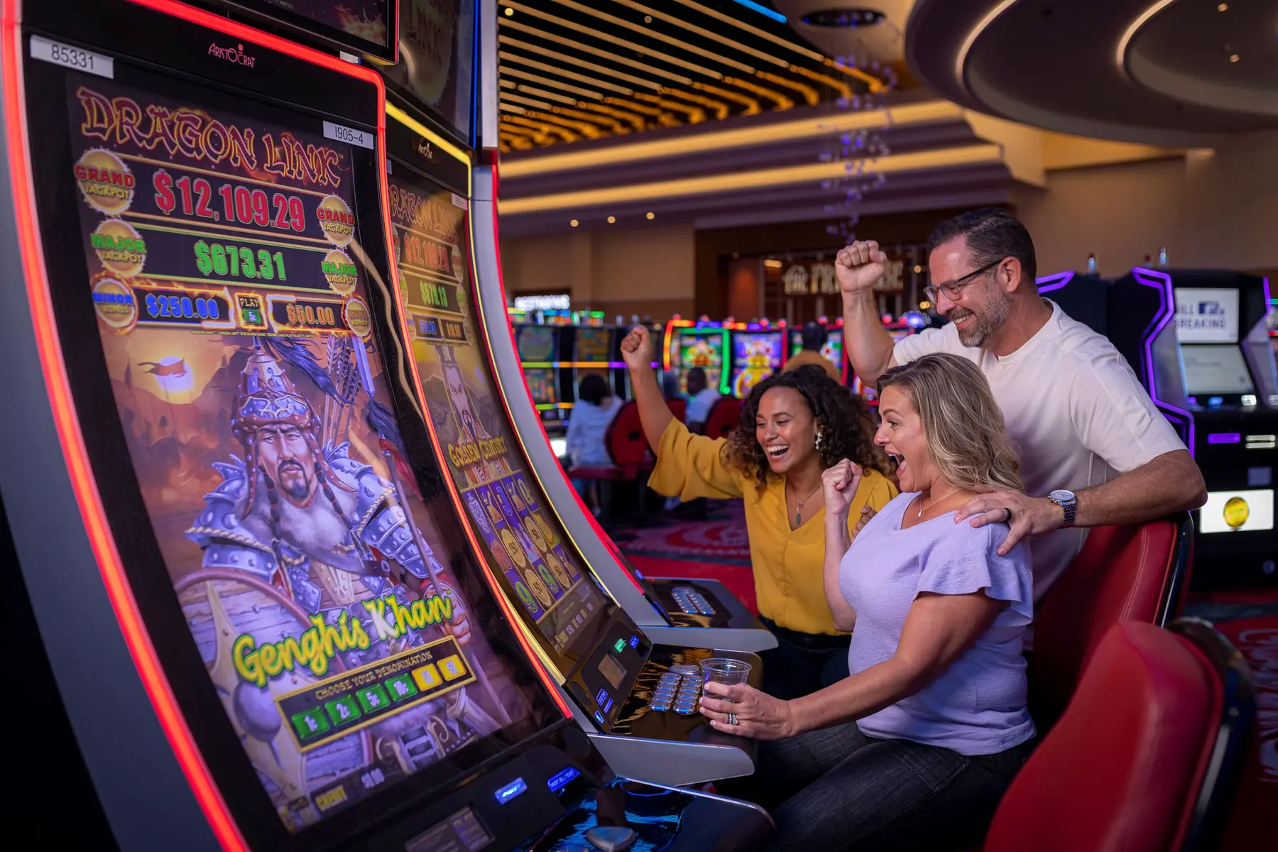 Excited people cheering while playing a Genghis Khan themed slot machine on a casino gaming floor