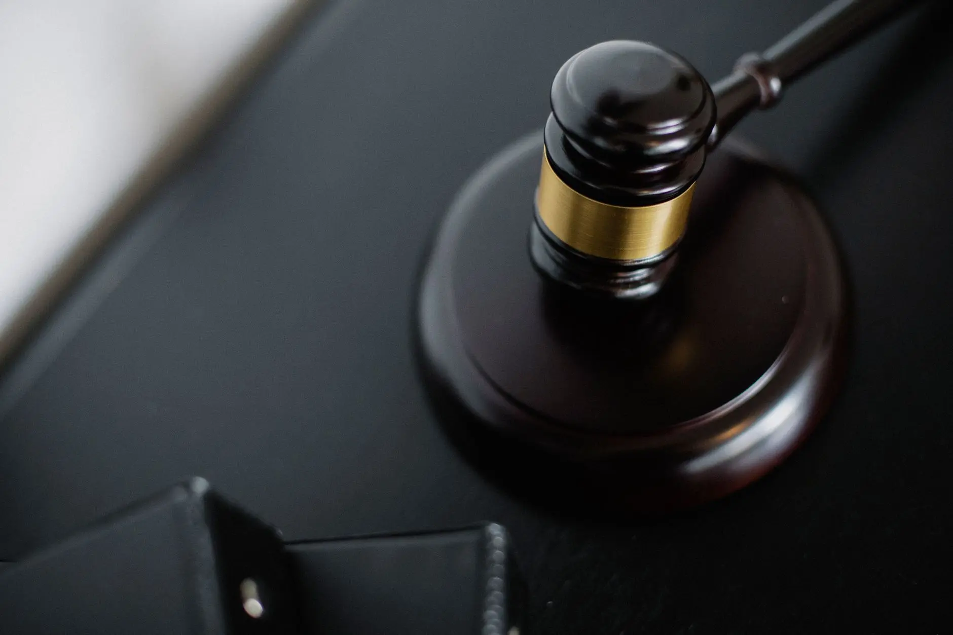 Close-up of a wooden courtroom gavel with a gold band on a dark desk surface.