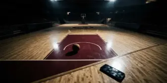 Empty basketball court with smartphone casting shadows under stadium lights