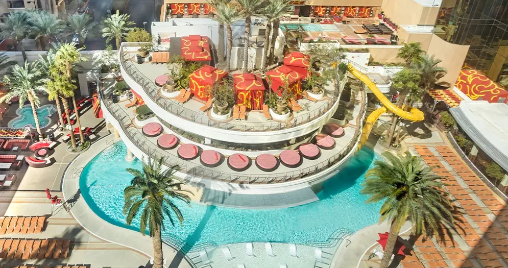 Aerial view of the multi-level pool deck at Golden Nugget Las Vegas with red cabanas and a yellow water slide.