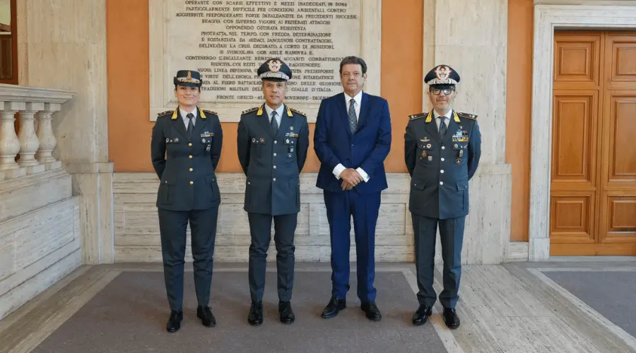 Three Guardia di Finanza officers in grey uniforms standing beside a man in a blue suit.