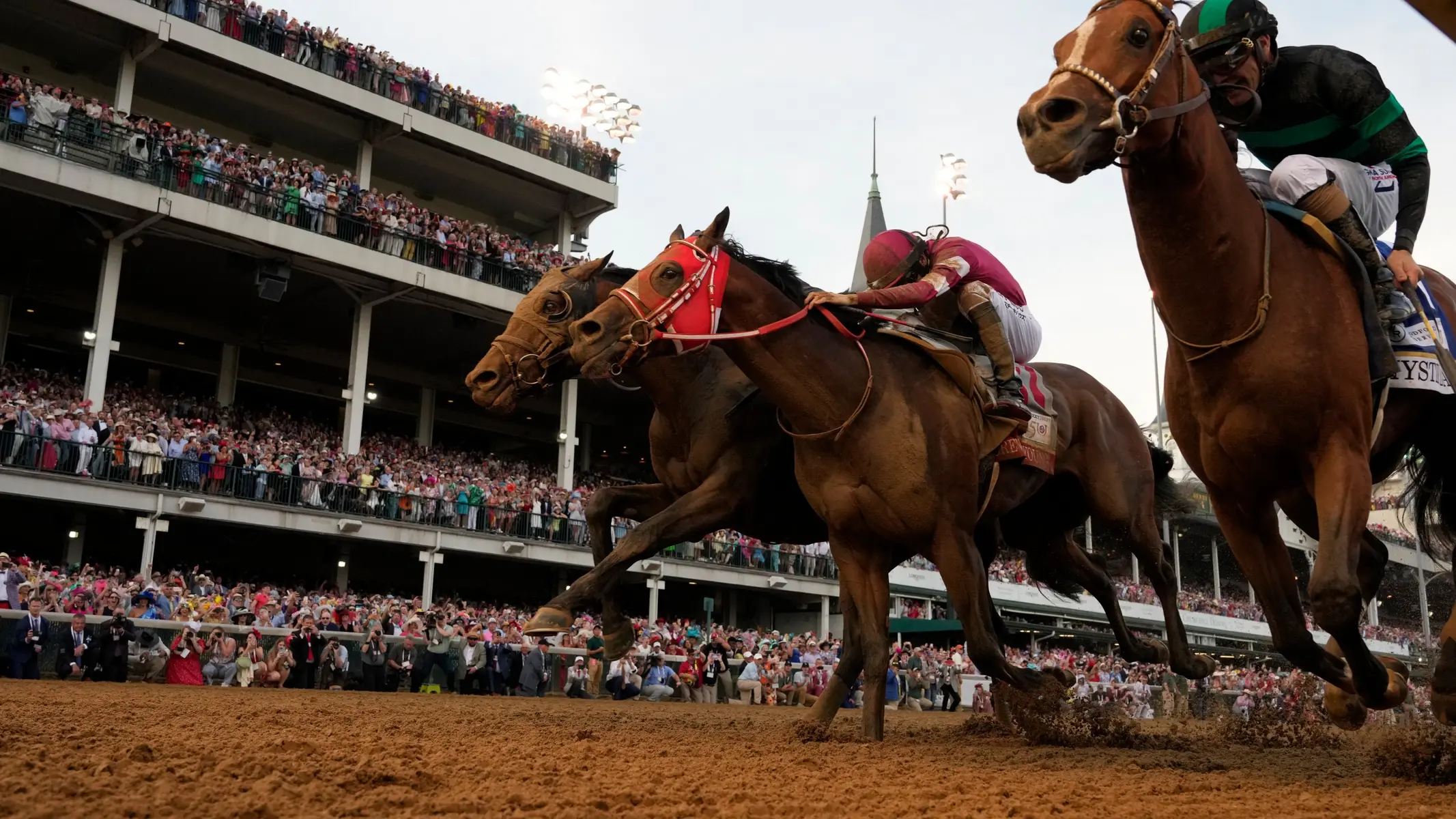 Three thoroughbred horses and their jockeys galloping toward the finish line at Churchill Downs.