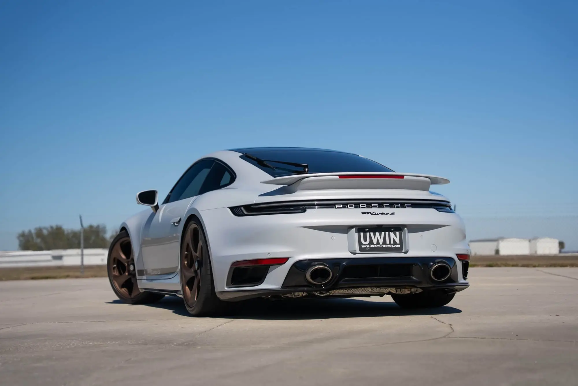 White Porsche 911 Turbo S parked on a pavement with clear blue sky.