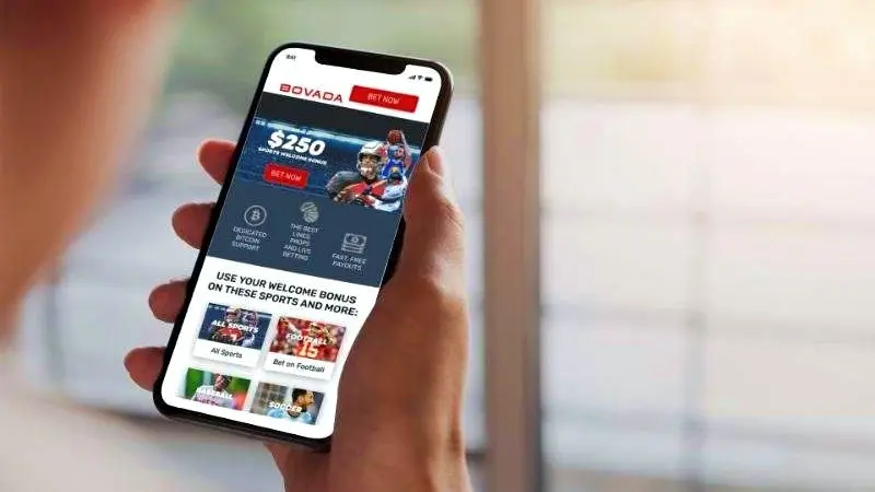 Close-up of a hand holding a phone displaying a sports betting app interface.