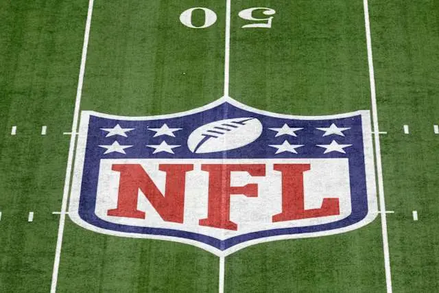 The NFL shield logo painted on the green grass of a football stadium field at the 50-yard line