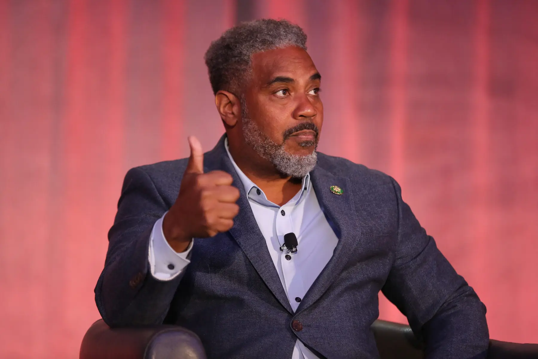 A man with grey hair and beard giving a thumbs up during a discussion.