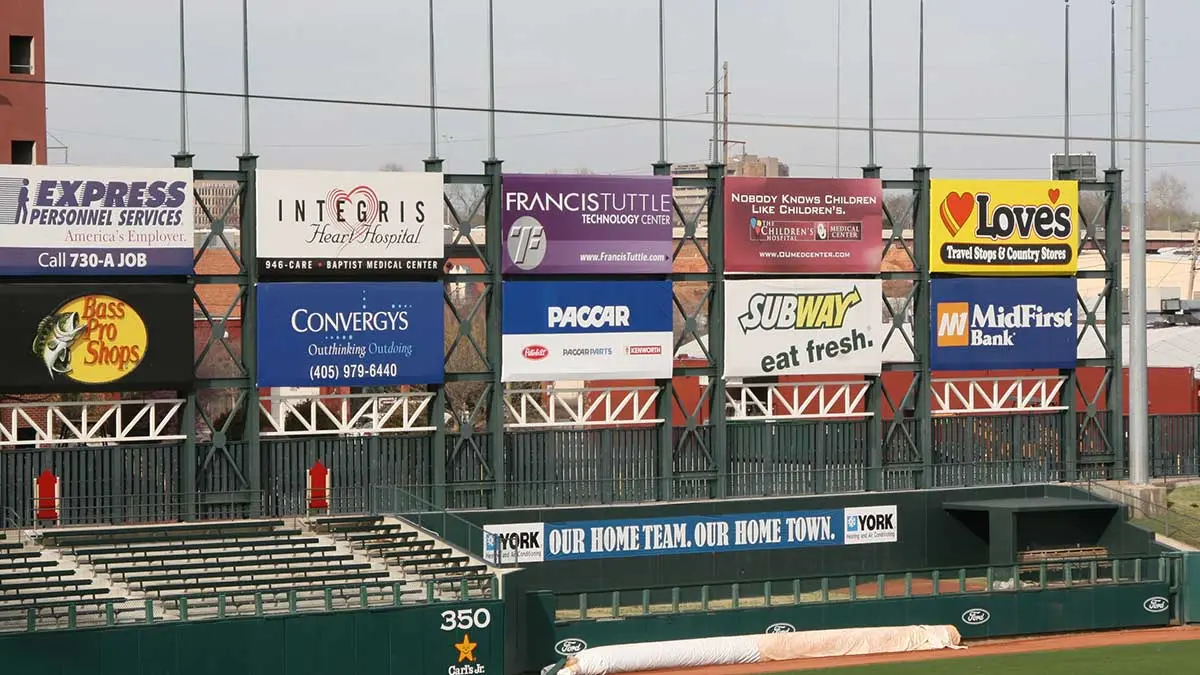 Multiple advertising boards at a stadium featuring various brands and services.