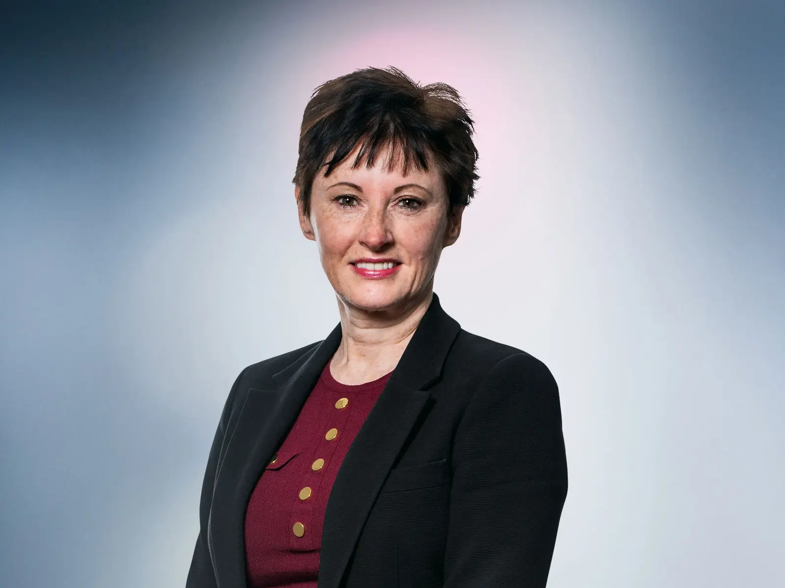 Professional portrait of a woman in a black blazer against a soft gradient background.