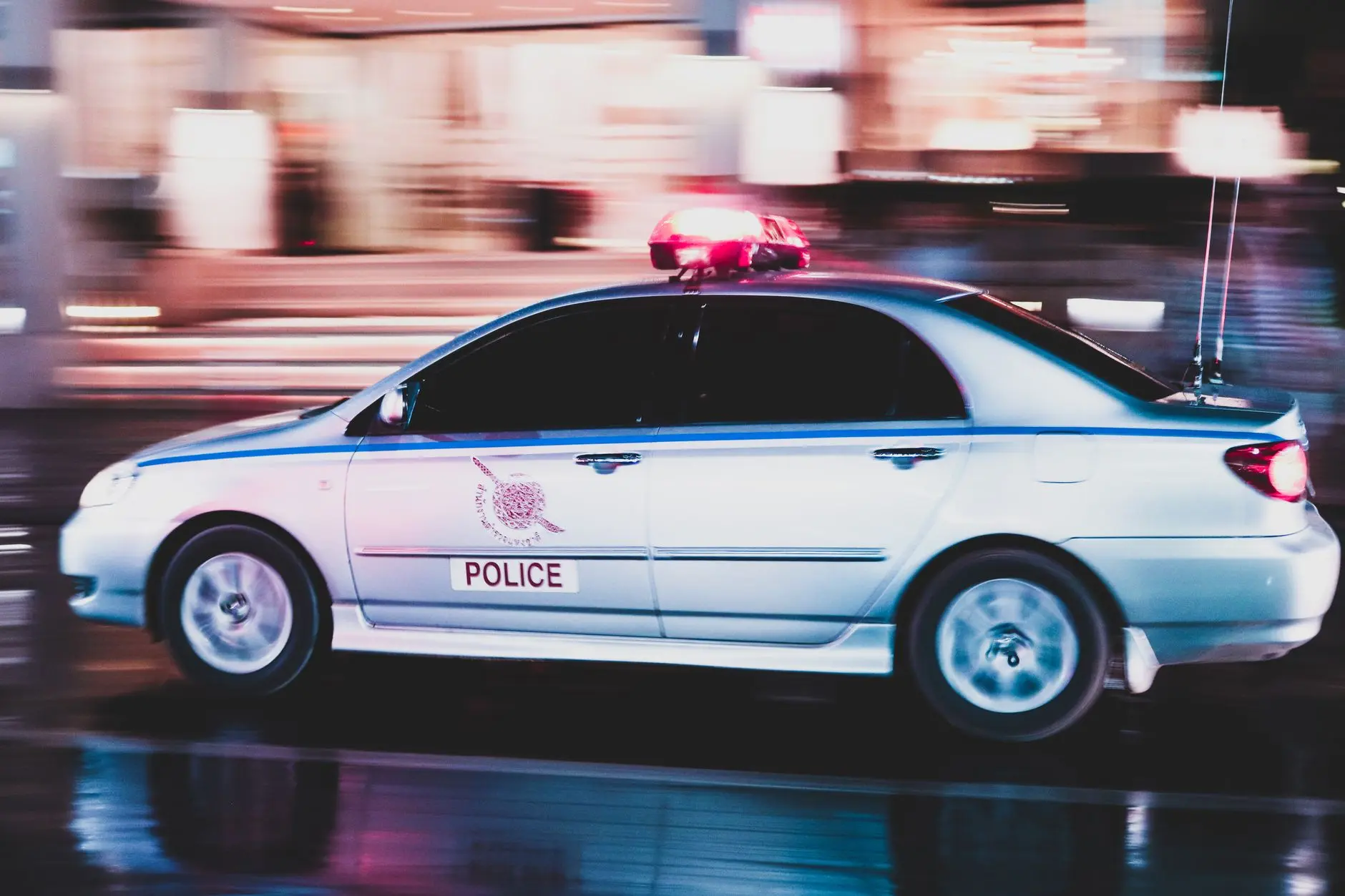 Taiwan police car in motion with flashing lights on a wet street at night.