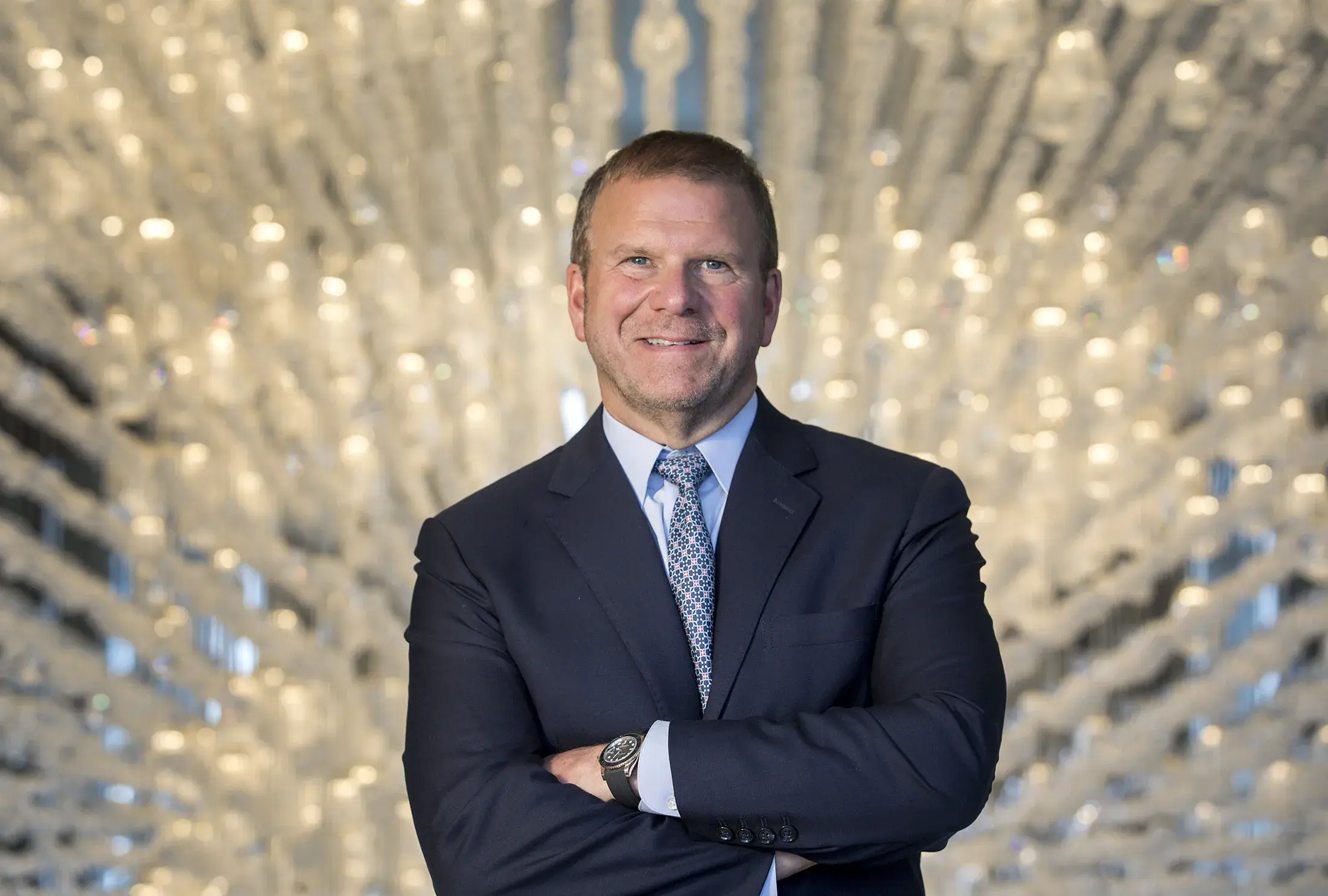 Businessman in a suit with arms crossed and a blurred sparkling background.