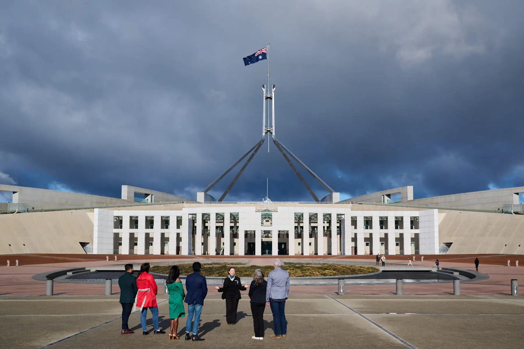 Wide shot of the Australian Parliament House in Canberra with people standing in the foreground under a moody sky