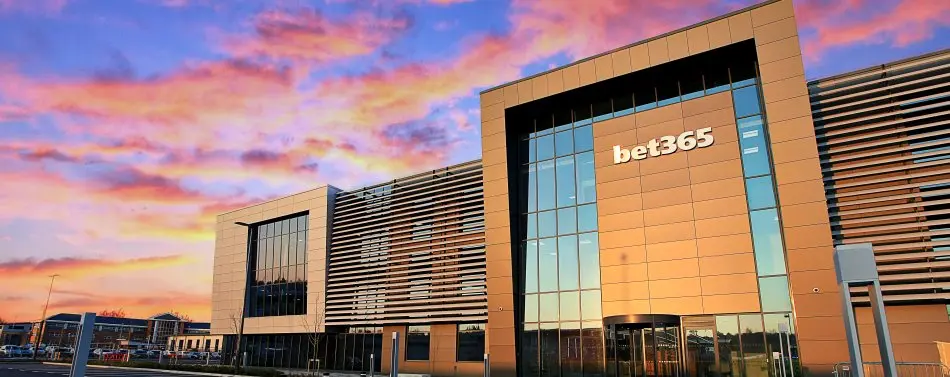 Modern bet365 headquarters building with gold cladding and glass facade under a colorful sunset sky
