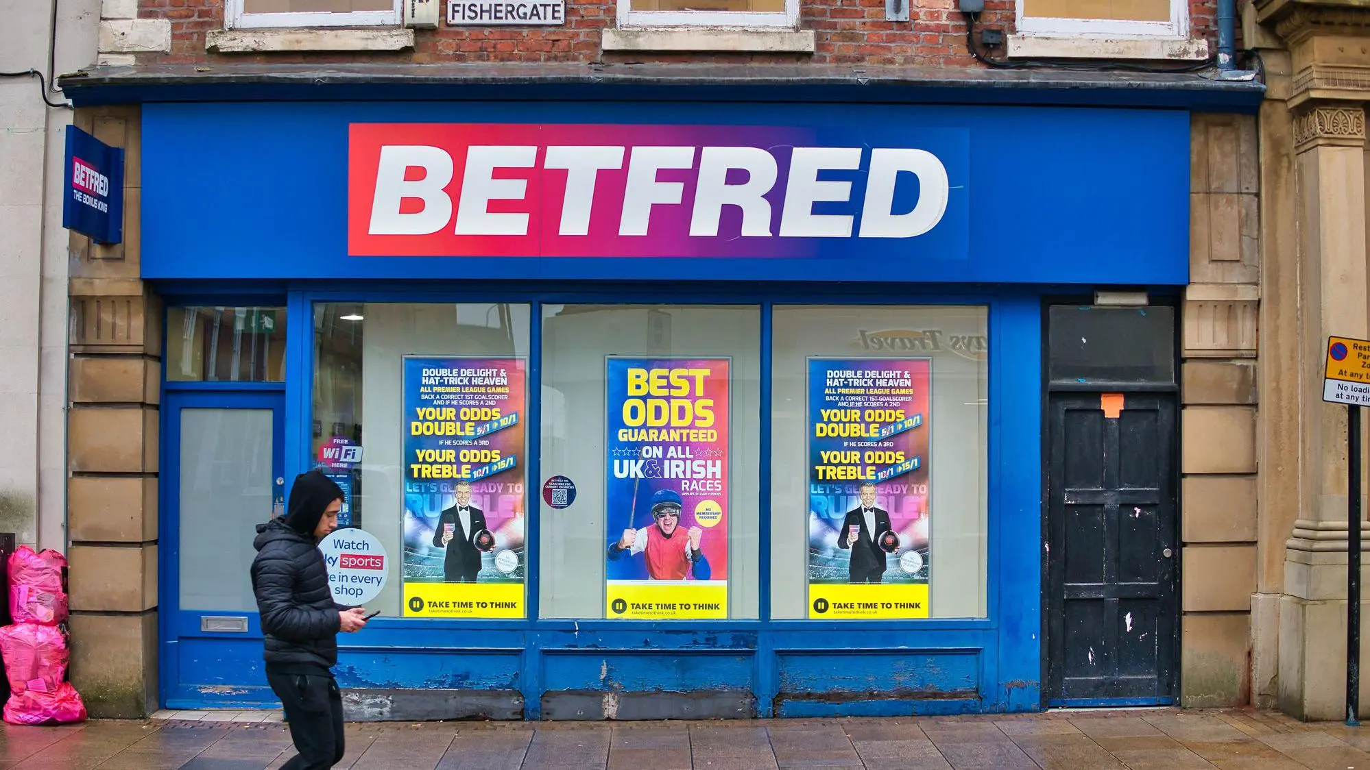 Exterior storefront of a Betfred betting shop on Fishergate street with blue branding and promotional posters.