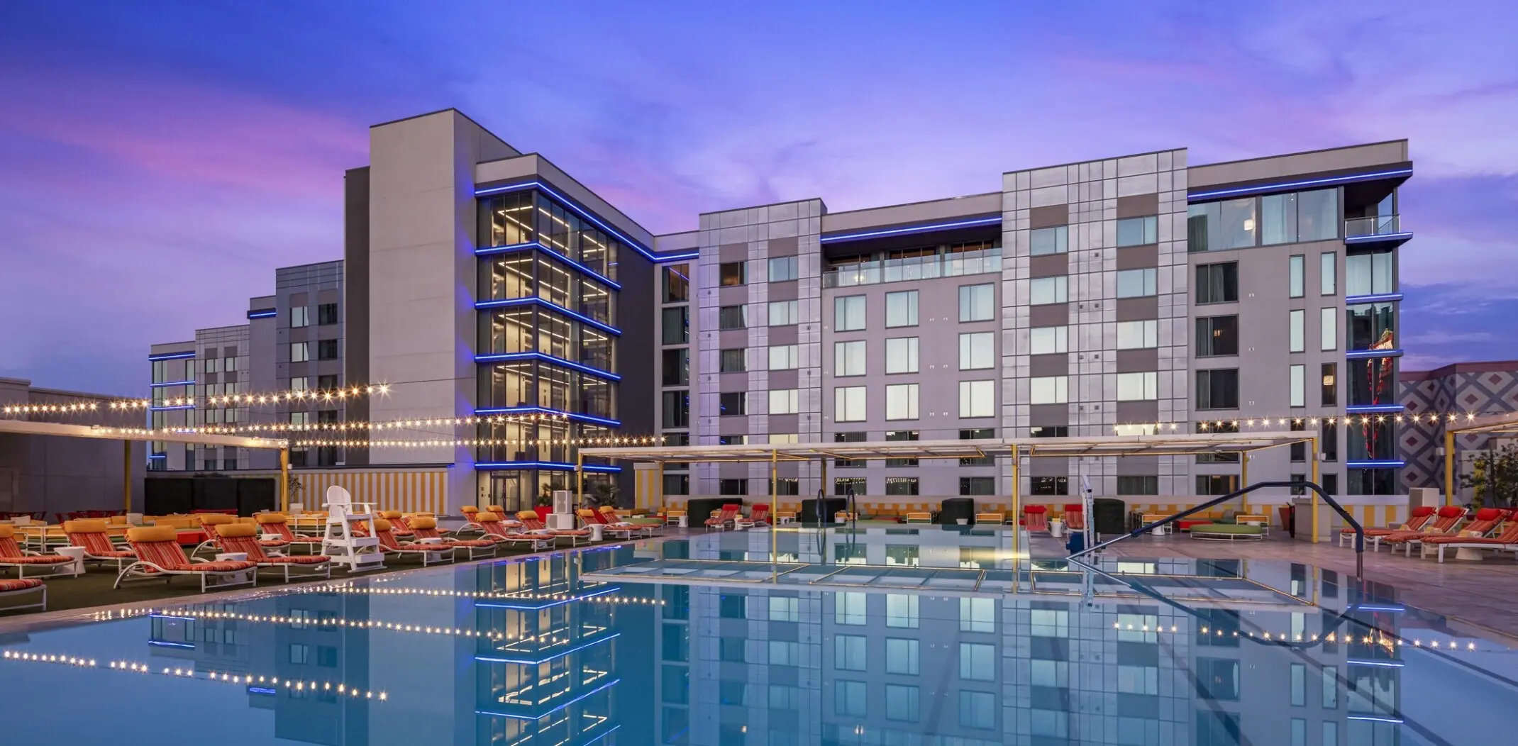 Modern hotel resort building with a luxury swimming pool and lounge chairs at twilight
