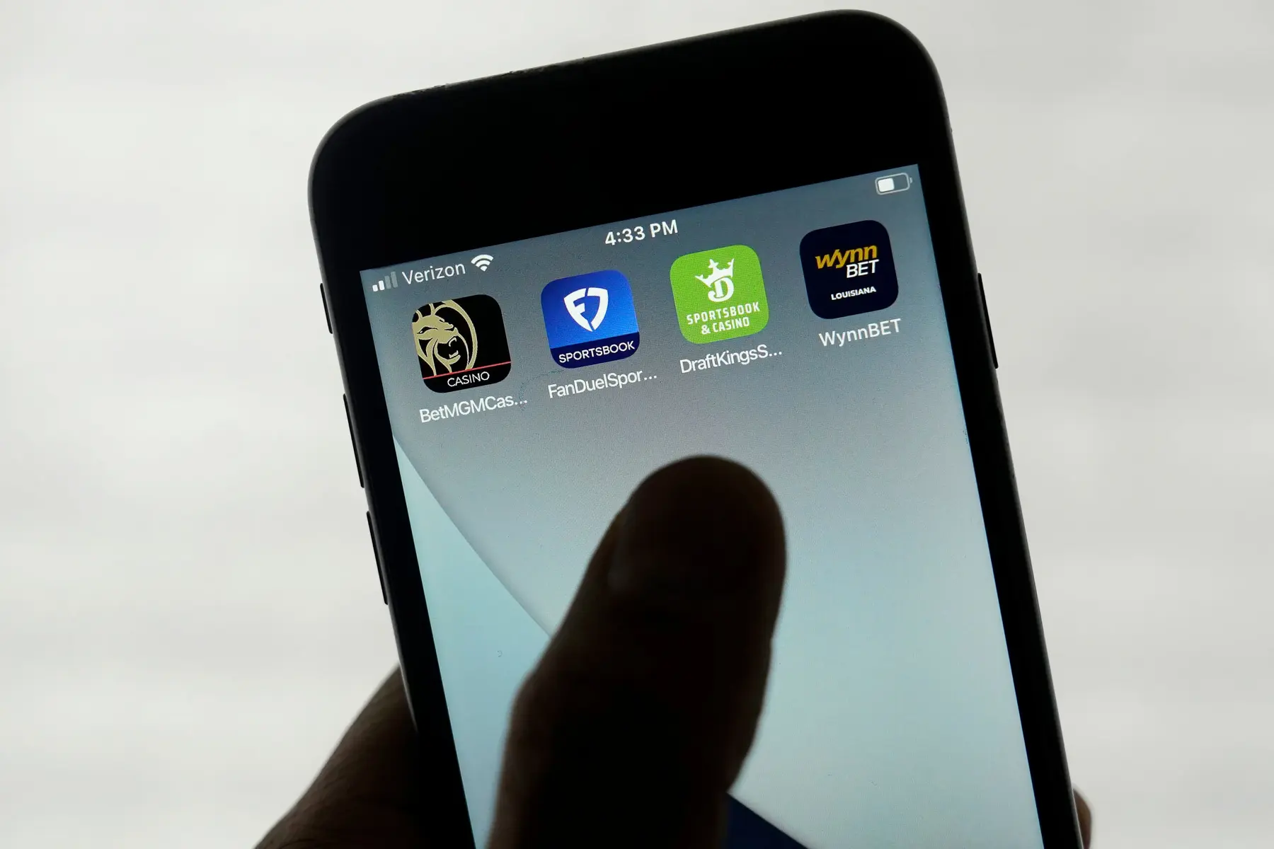 A close-up of a smartphone screen displaying sports betting apps including BetMGM, FanDuel, DraftKings, and WynnBET