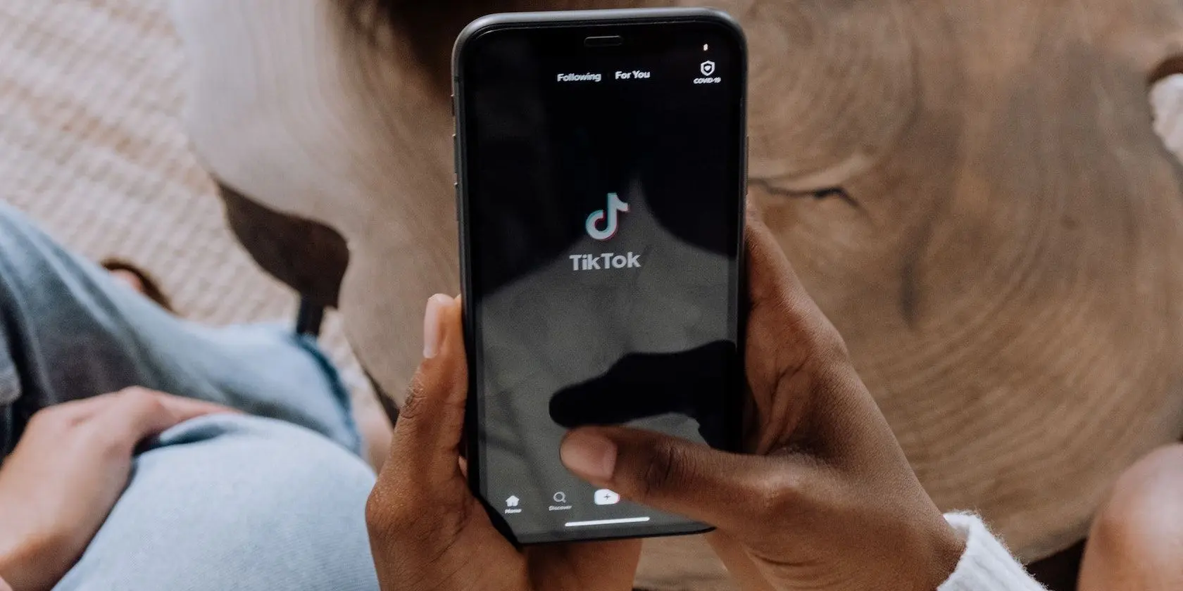 Close-up of hands holding a smartphone displaying the TikTok app interface on a black screen.