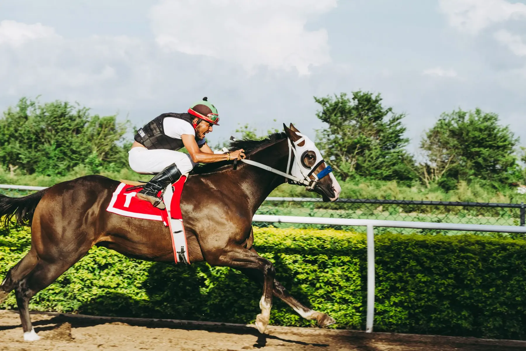 A jockey in white and black racing gear riding a brown racehorse at high speed on a dirt track.