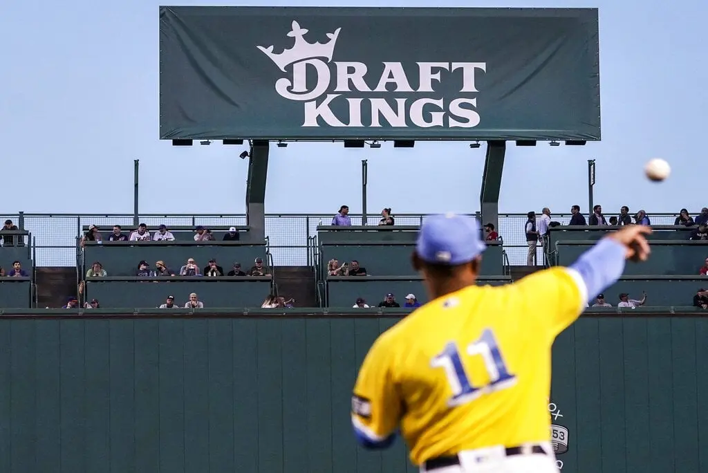 A baseball player in a yellow jersey throwing a ball with a large DraftKings advertisement in the background.