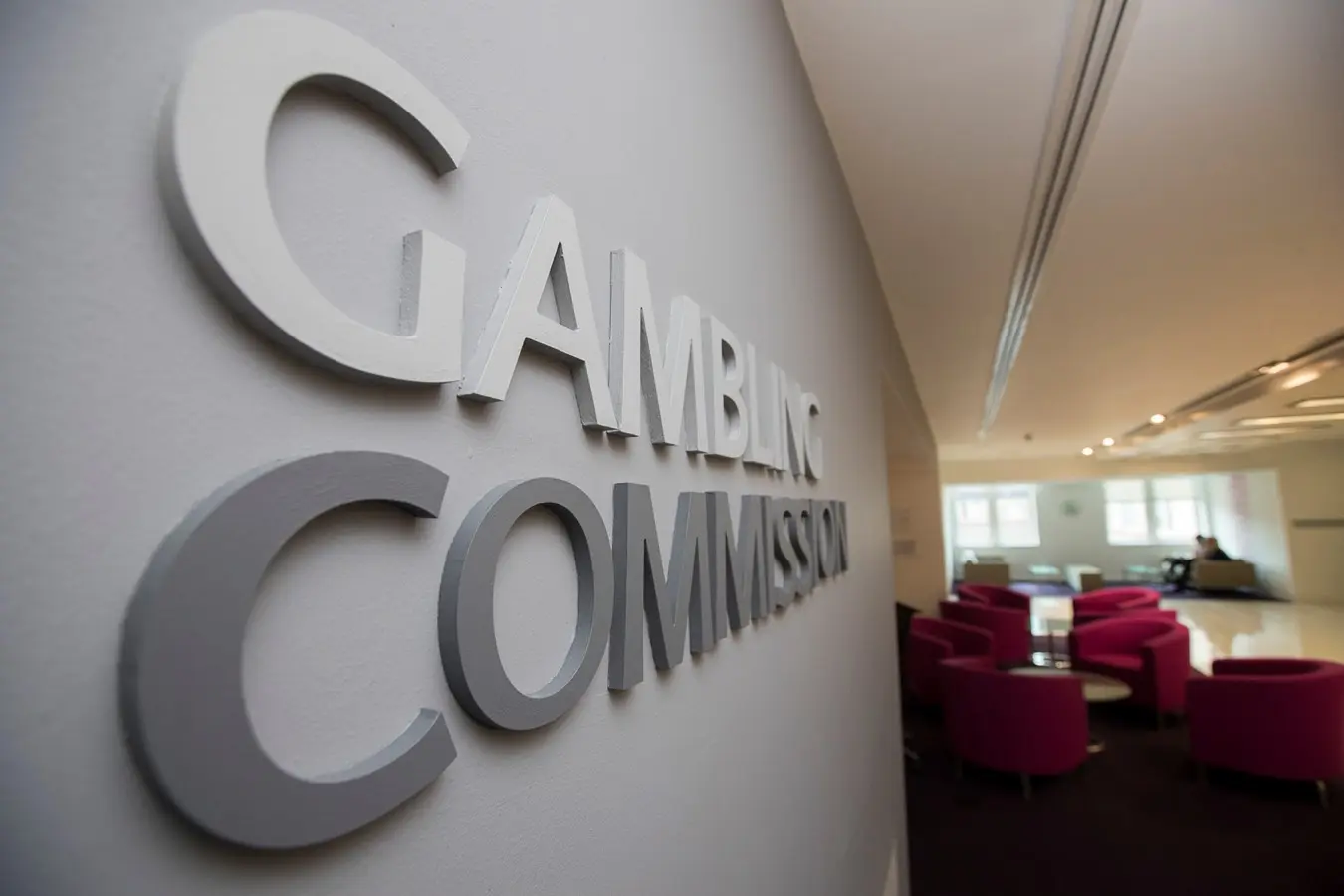 Close-up of the Gambling Commission signage on a grey office wall with a waiting area in the background.