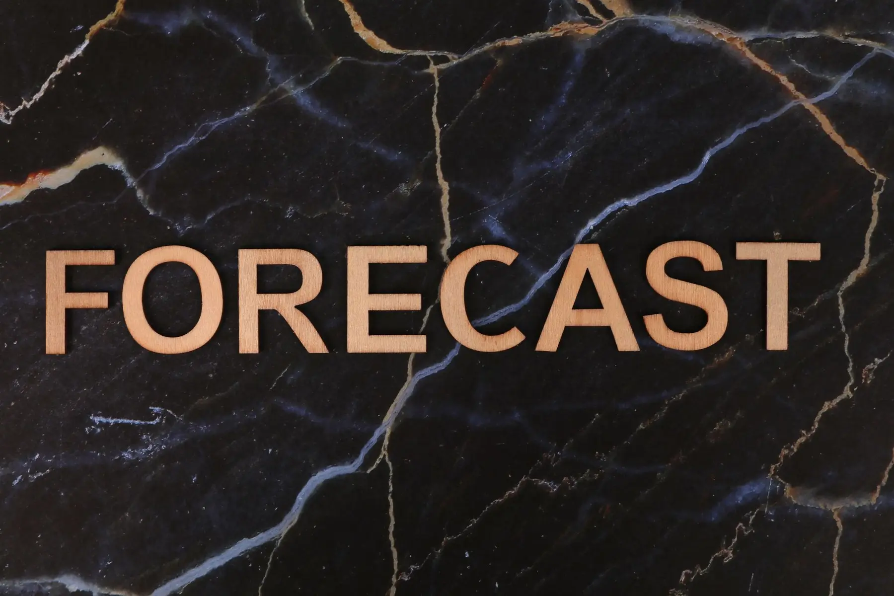 Wooden letters spelling 'FORECAST' on a dark marble background with gold veins