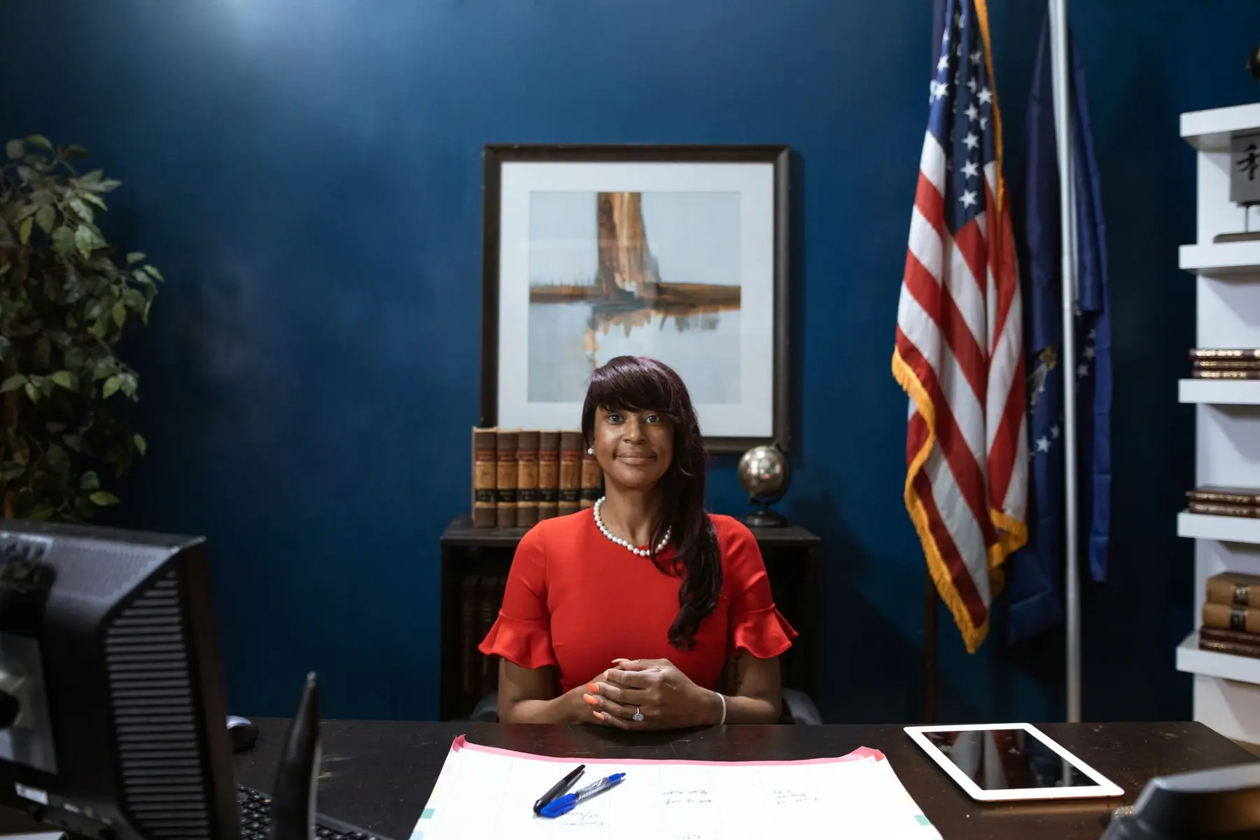 Portrait of Kris Mayes, Arizona Attorney General, sitting at her desk in an office with a US flag.