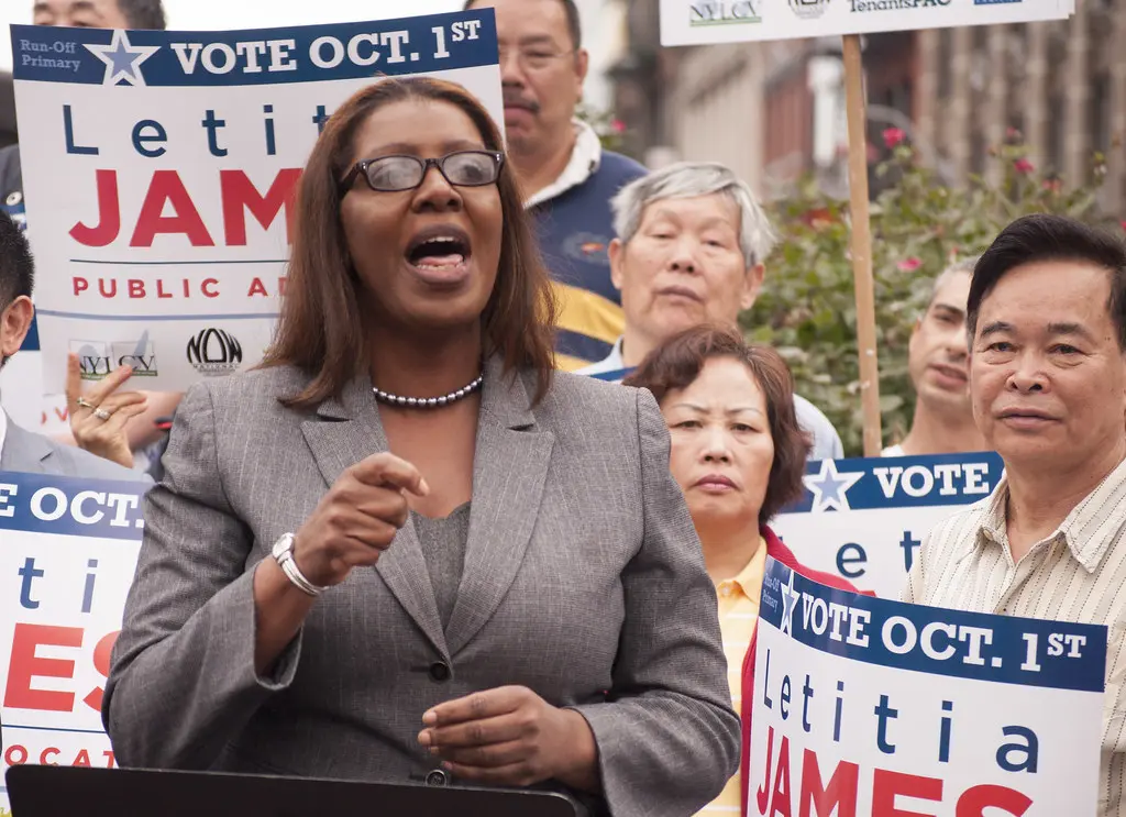Letitia James speaking at a campaign event with supporters holding signs.