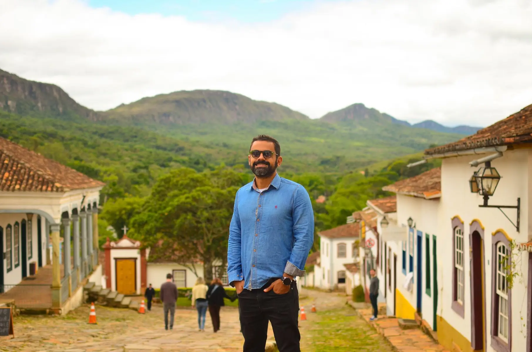 Senator Alessandro Vieira wearing sunglasses and a blue shirt, standing in a historic Brazilian town street.